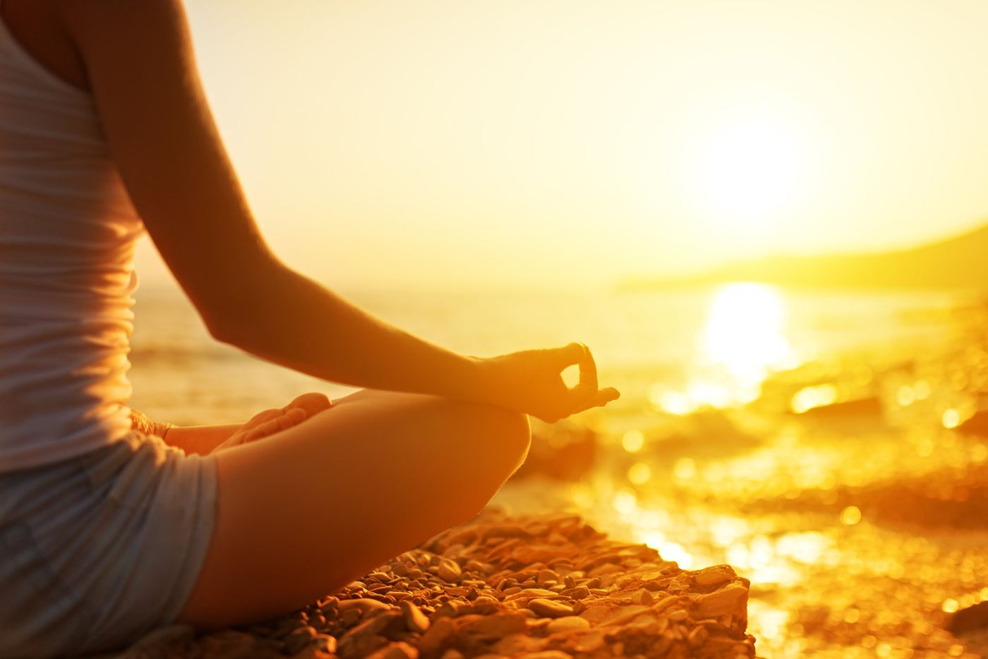A woman meditating cross-legged on a beach at sunset